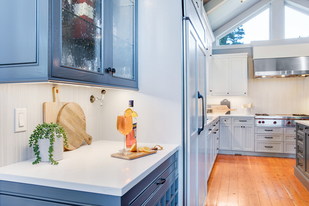Idée de décoration pour une grande cuisine américaine en U avec un évier encastré, un placard à porte affleurante, des portes de placard grises, un plan de travail en quartz modifié, une crédence grise, une crédence en carreau de porcelaine, un électroménager en acier inoxydable, un sol en bois brun, îlot, un sol marron, un plan de travail blanc et un plafond voûté.