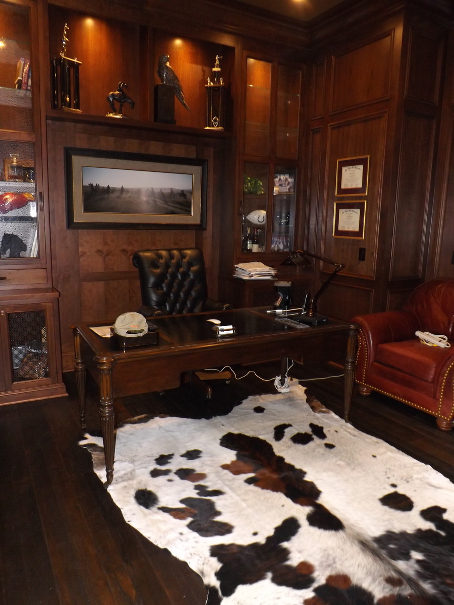 Large traditional study room in Other with dark hardwood floors, a standard fireplace, a wood fireplace surround, a freestanding desk, brown walls and brown floor.