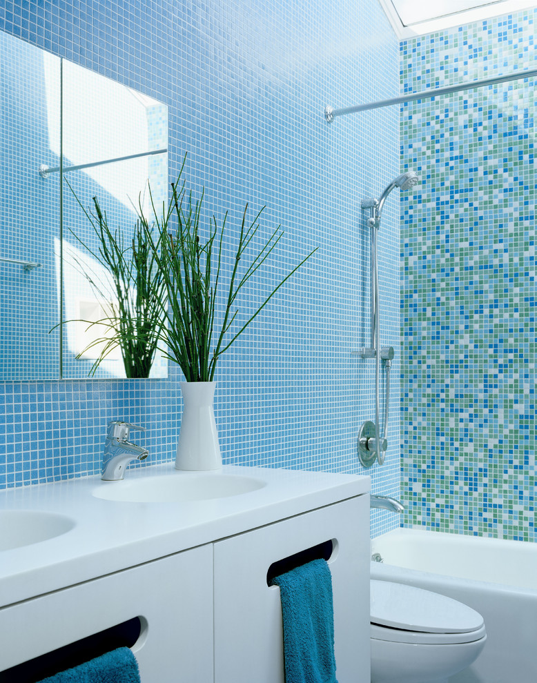 Inspiration for a small contemporary bathroom in San Francisco with mosaic tile, flat-panel cabinets, white cabinets, an alcove tub, a shower/bathtub combo, a two-piece toilet, blue tile, blue walls, an integrated sink, solid surface benchtops and mosaic tile floors.