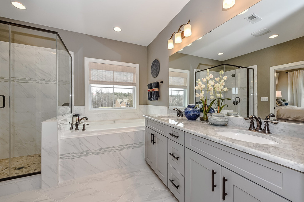 This is an example of a mid-sized transitional master bathroom in Charlotte with recessed-panel cabinets, grey cabinets, a drop-in tub, an alcove shower, porcelain tile, grey walls, porcelain floors, quartzite benchtops, white tile, a hinged shower door, an undermount sink, grey floor and grey benchtops.