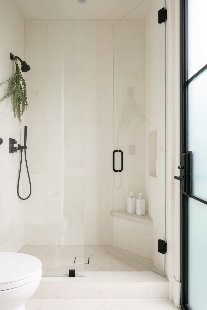 Пример оригинального дизайна: большая ванная комната в средиземноморском стиле с плоскими фасадами, светлыми деревянными фасадами, душем в нише, бежевой плиткой, плиткой из известняка, полом из известняка, мраморной столешницей, бежевым полом, душем с распашными дверями, белой столешницей, сиденьем для душа, тумбой под одну раковину и встроенной тумбой