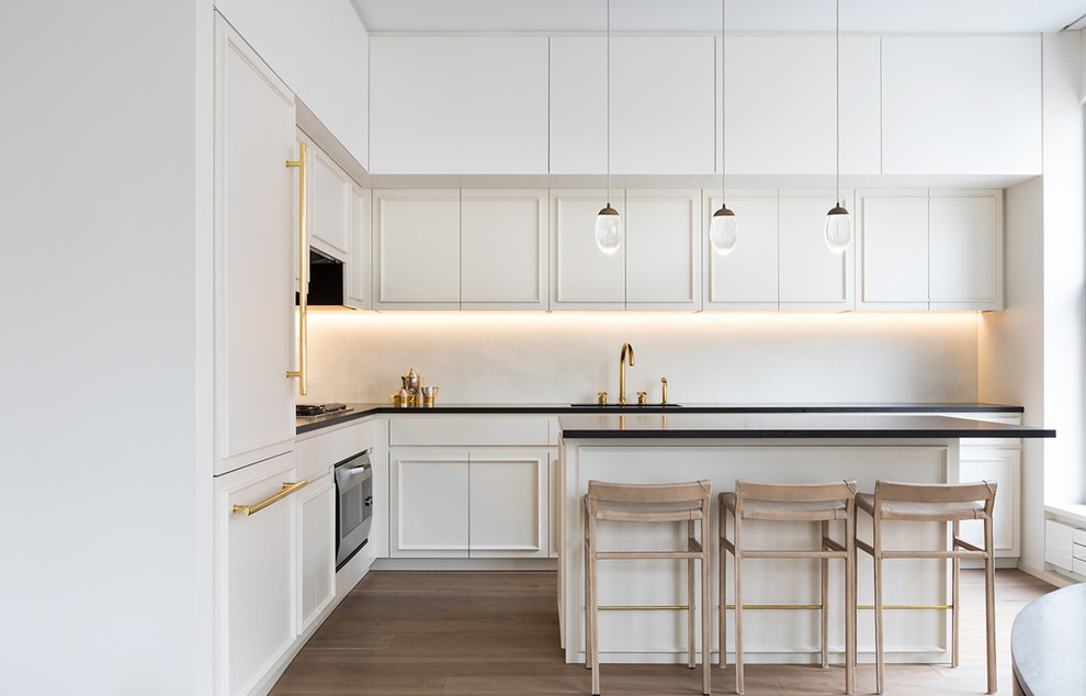 Inspiration for a mid-sized contemporary u-shaped eat-in kitchen in New York with an undermount sink, flat-panel cabinets, white cabinets, soapstone benchtops, white splashback, stone slab splashback, panelled appliances, light hardwood floors, with island, beige floor and black benchtop.