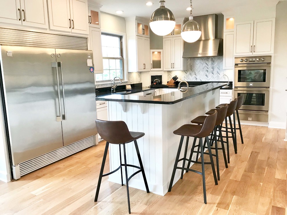 Open concept kitchen - large transitional u-shaped light wood floor open concept kitchen idea with an undermount sink, raised-panel cabinets, white cabinets, granite countertops, multicolored backsplash, marble backsplash, stainless steel appliances, an island and black countertops