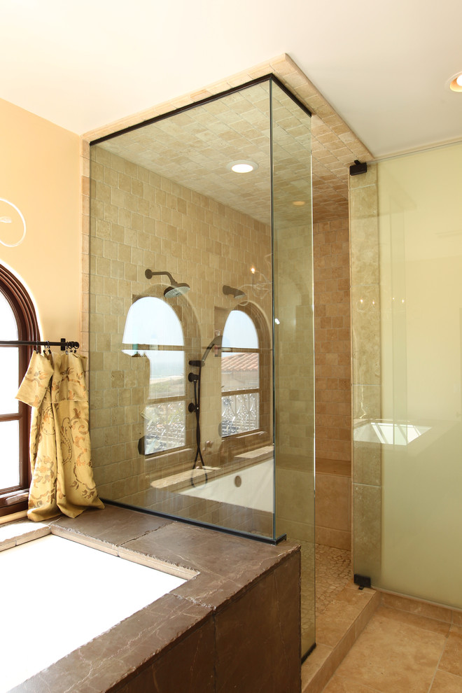 Inspiration for a large mediterranean master bathroom in Los Angeles with beige walls, travertine floors, furniture-like cabinets, distressed cabinets, an undermount tub, a double shower, a two-piece toilet, beige tile, travertine, a vessel sink, wood benchtops, beige floor and a hinged shower door.