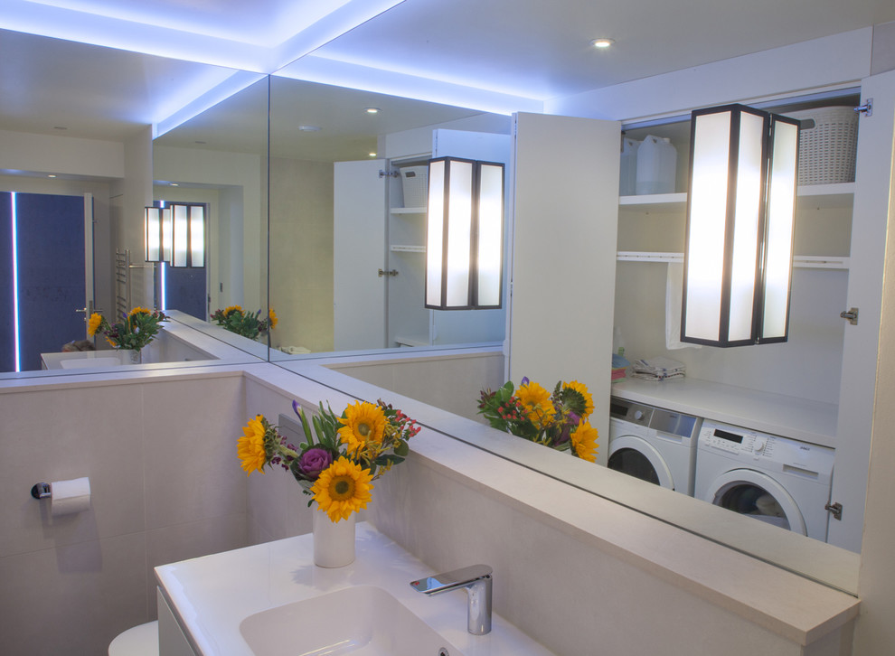 This is an example of a mid-sized contemporary bathroom in London with an integrated sink, white cabinets, solid surface benchtops, a wall-mount toilet, ceramic tile and ceramic floors.