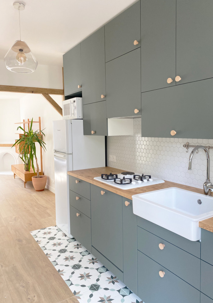 Mid-sized contemporary galley open plan kitchen in Paris with a single-bowl sink, beaded inset cabinets, green cabinets, wood benchtops, white splashback, ceramic splashback, panelled appliances, light hardwood floors, brown floor, brown benchtop and exposed beam.