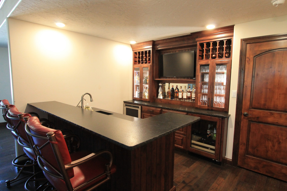 Inspiration for a large rustic wet bar remodel with an undermount sink, raised-panel cabinets, medium tone wood cabinets, granite countertops and black countertops