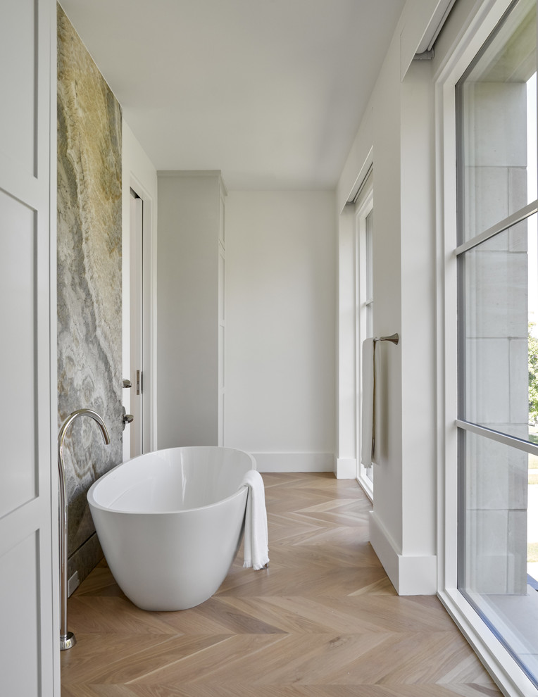 This is an example of a mid-sized transitional master bathroom in Dallas with a freestanding tub, white walls, light hardwood floors, shaker cabinets, beige cabinets, a curbless shower, gray tile, white tile, porcelain tile, marble benchtops, brown floor, a hinged shower door and white benchtops.