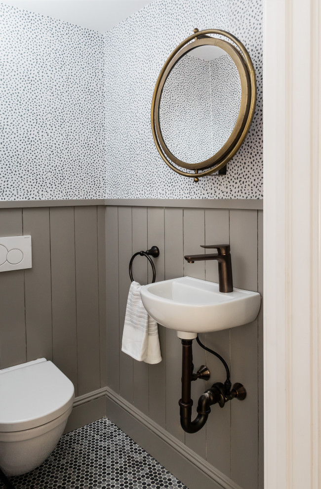 Mid-sized transitional powder room in Boston with recessed-panel cabinets, white cabinets, a wall-mount toilet, gray tile, wood-look tile, multi-coloured walls, pebble tile floors, a wall-mount sink, solid surface benchtops, multi-coloured floor, white benchtops and wallpaper.