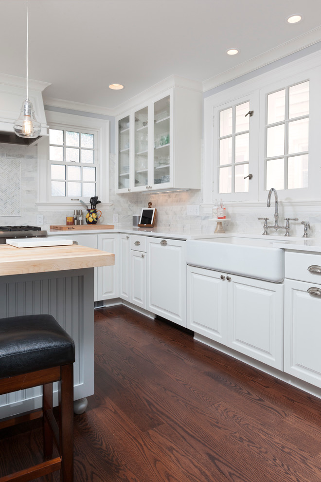Inspiration for a mid-sized country l-shaped kitchen pantry in Milwaukee with a farmhouse sink, flat-panel cabinets, white cabinets, wood benchtops, white splashback, stone tile splashback, stainless steel appliances, dark hardwood floors and with island.