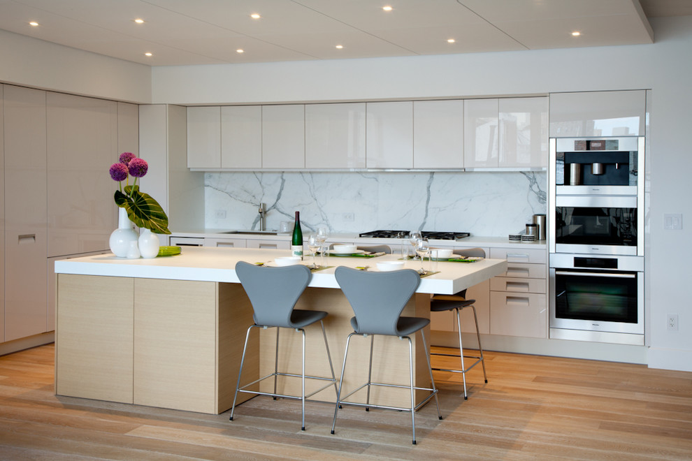 This is an example of a modern galley kitchen in New York with flat-panel cabinets, white cabinets, white splashback and stone slab splashback.