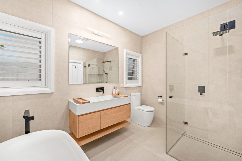Exemple d'une salle de bain principale bord de mer en bois clair de taille moyenne avec une baignoire indépendante, une douche d'angle, un carrelage beige, un lavabo intégré, une cabine de douche à porte battante, un plan de toilette blanc, meuble simple vasque et meuble-lavabo suspendu.