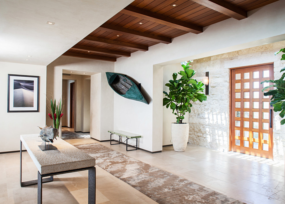 Inspiration for a tropical foyer in Orange County with white walls, a single front door, a medium wood front door and beige floor.