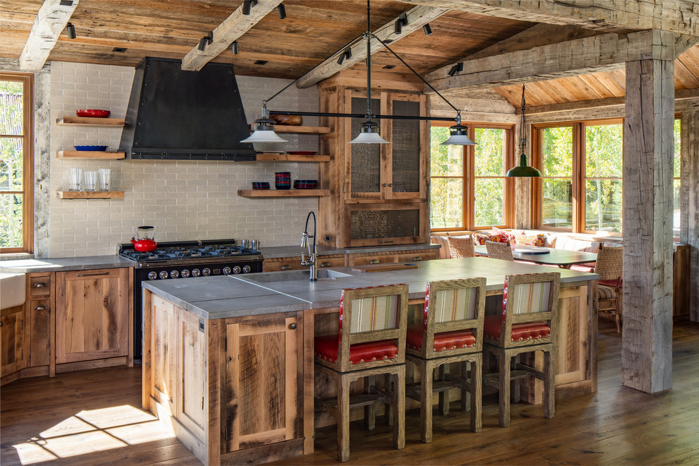 Example of a mountain style l-shaped dark wood floor and brown floor kitchen design with a farmhouse sink, shaker cabinets, medium tone wood cabinets, gray backsplash, black appliances, an island and gray countertops