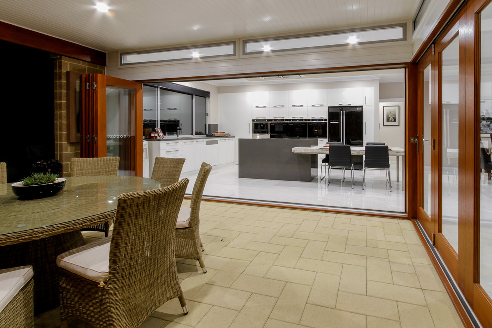 Large contemporary l-shaped eat-in kitchen in Other with a double-bowl sink, flat-panel cabinets, white cabinets, quartz benchtops, grey splashback, glass sheet splashback, black appliances, ceramic floors and with island.