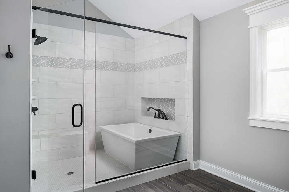This is an example of a large country master wet room bathroom in Chicago with shaker cabinets, distressed cabinets, a freestanding tub, a two-piece toilet, white tile, ceramic tile, grey walls, ceramic floors, an undermount sink, engineered quartz benchtops, black floor, a hinged shower door and white benchtops.