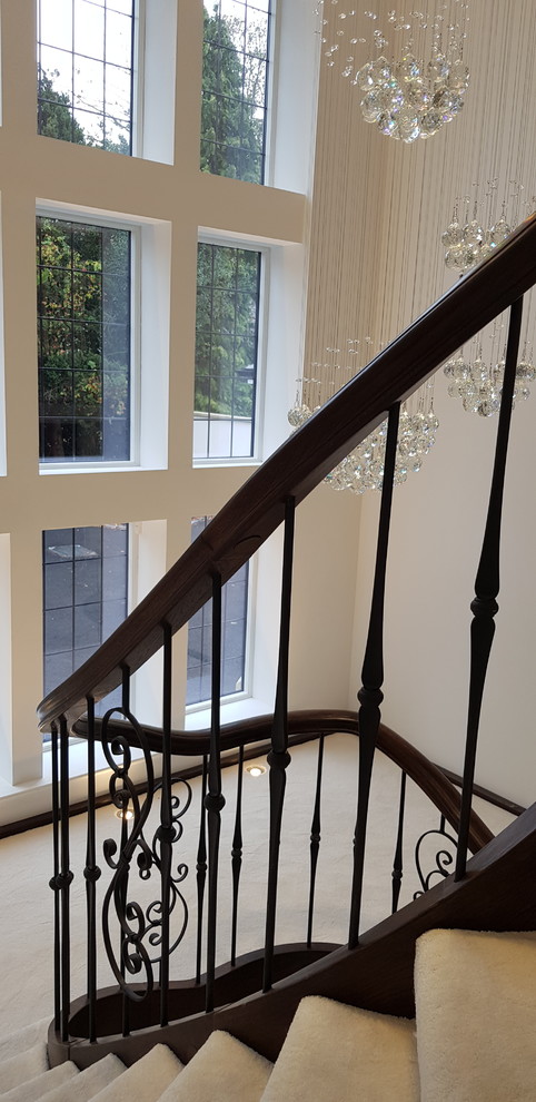 This is an example of a large traditional wood curved staircase in Cheshire with wood risers and metal railing.