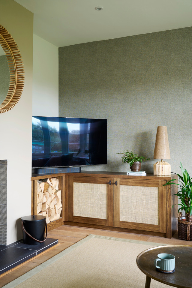 Cette image montre un salon nordique de taille moyenne et ouvert avec un bar de salon, un mur vert, un sol en bois brun, un poêle à bois, un manteau de cheminée en plâtre, un téléviseur d'angle, un sol marron et du papier peint.