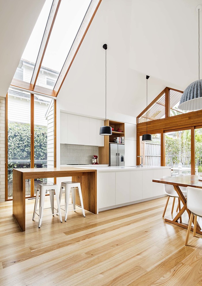 Modern galley eat-in kitchen in Melbourne with flat-panel cabinets, white cabinets, grey splashback, stainless steel appliances, light hardwood floors and with island.