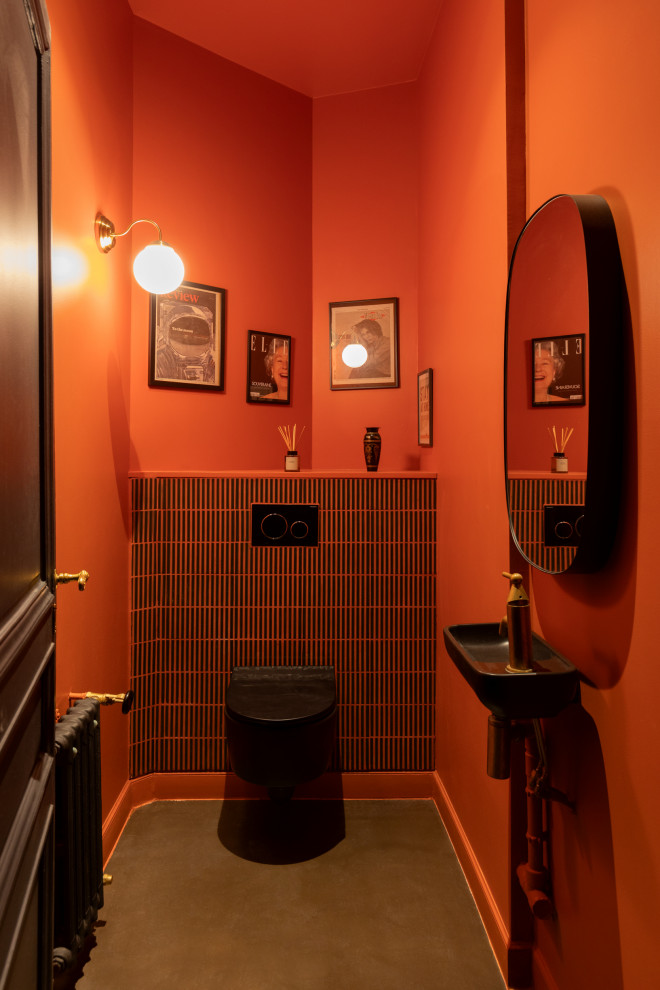 Inspiration för ett funkis toalett, med en vägghängd toalettstol, svart kakel, orange väggar, betonggolv, ett väggmonterat handfat och grått golv