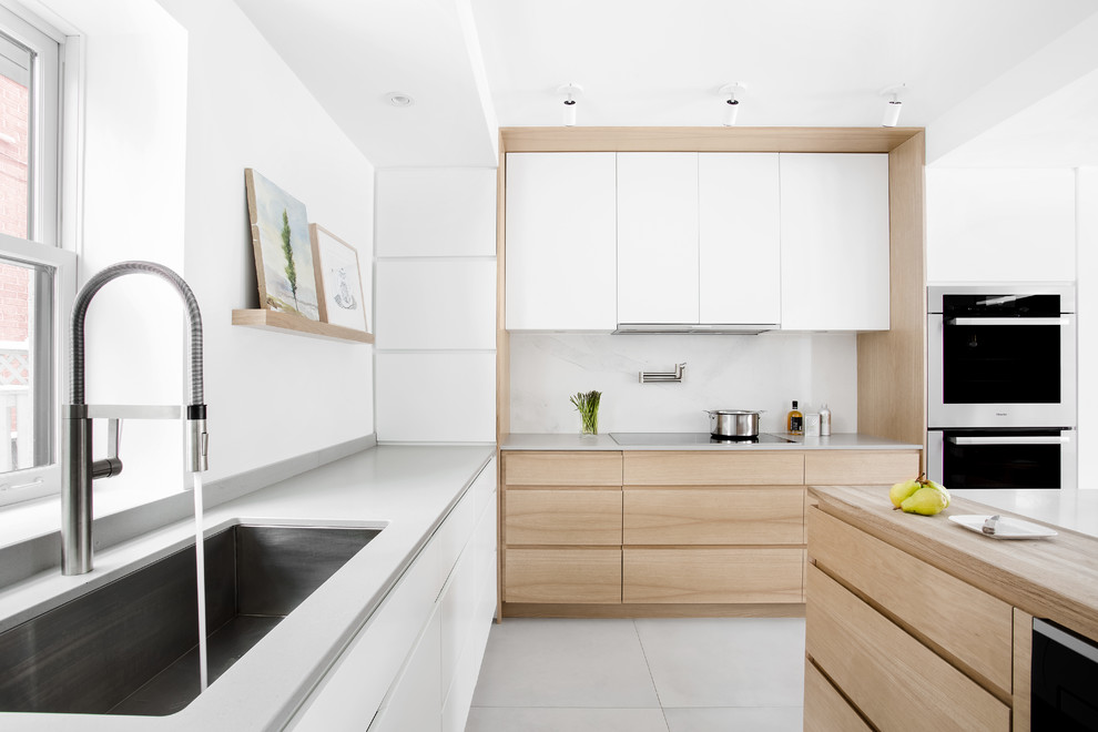 Mid-sized modern u-shaped eat-in kitchen in Montreal with an undermount sink, flat-panel cabinets, light wood cabinets, quartz benchtops, panelled appliances, porcelain floors and with island.