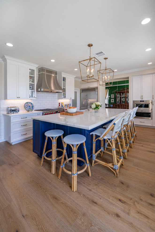 This is an example of a large modern l-shaped eat-in kitchen in San Diego with an integrated sink, recessed-panel cabinets, white cabinets, quartz benchtops, white splashback, subway tile splashback, stainless steel appliances, light hardwood floors, with island, brown floor and white benchtop.