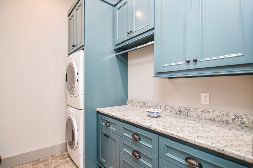 Inspiration for a mid-sized mediterranean single-wall dedicated laundry room in Other with beaded inset cabinets, solid surface benchtops, white walls, brick floors, multi-coloured floor, green benchtop, blue cabinets and a stacked washer and dryer.