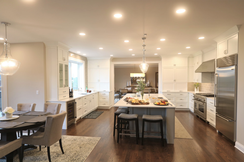 Example of a huge transitional u-shaped dark wood floor and brown floor eat-in kitchen design in Cincinnati with an undermount sink, recessed-panel cabinets, white cabinets, quartz countertops, beige backsplash, subway tile backsplash, stainless steel appliances, an island and white countertops