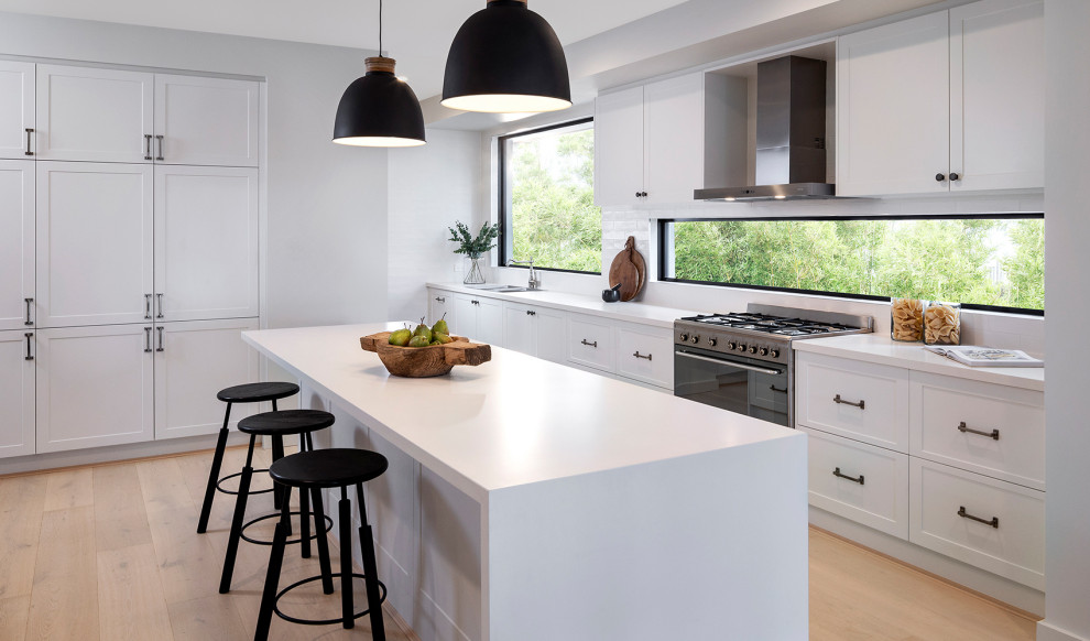 Photo of a large contemporary l-shaped kitchen in Other with a double-bowl sink, recessed-panel cabinets, white cabinets, mirror splashback, panelled appliances, with island, black floor and white benchtop.