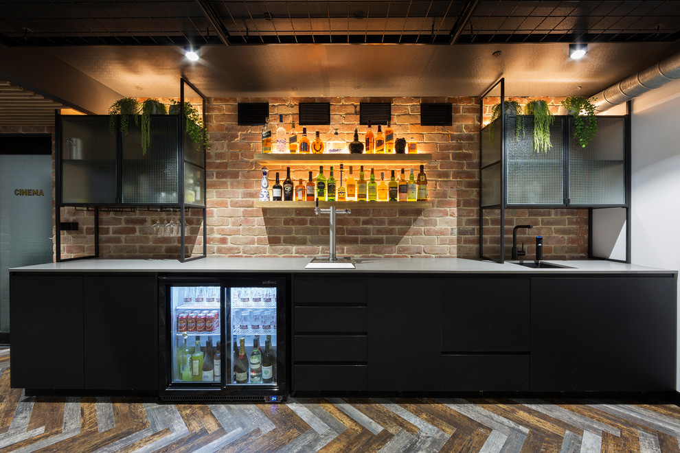 This is an example of a mid-sized contemporary single-wall wet bar in Canberra - Queanbeyan with an undermount sink, flat-panel cabinets, black cabinets, quartz benchtops, brick splashback, vinyl floors, multi-coloured floor, grey benchtop and red splashback.