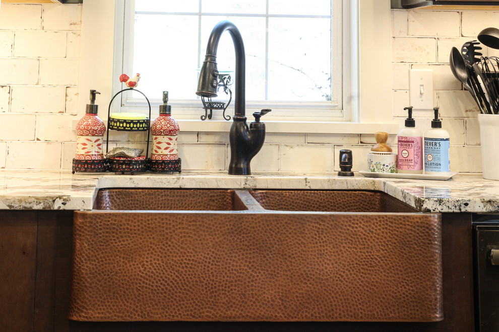 Example of a mid-sized mountain style l-shaped vinyl floor and brown floor enclosed kitchen design with a farmhouse sink, shaker cabinets, dark wood cabinets, granite countertops, white backsplash, ceramic backsplash, stainless steel appliances, an island and white countertops
