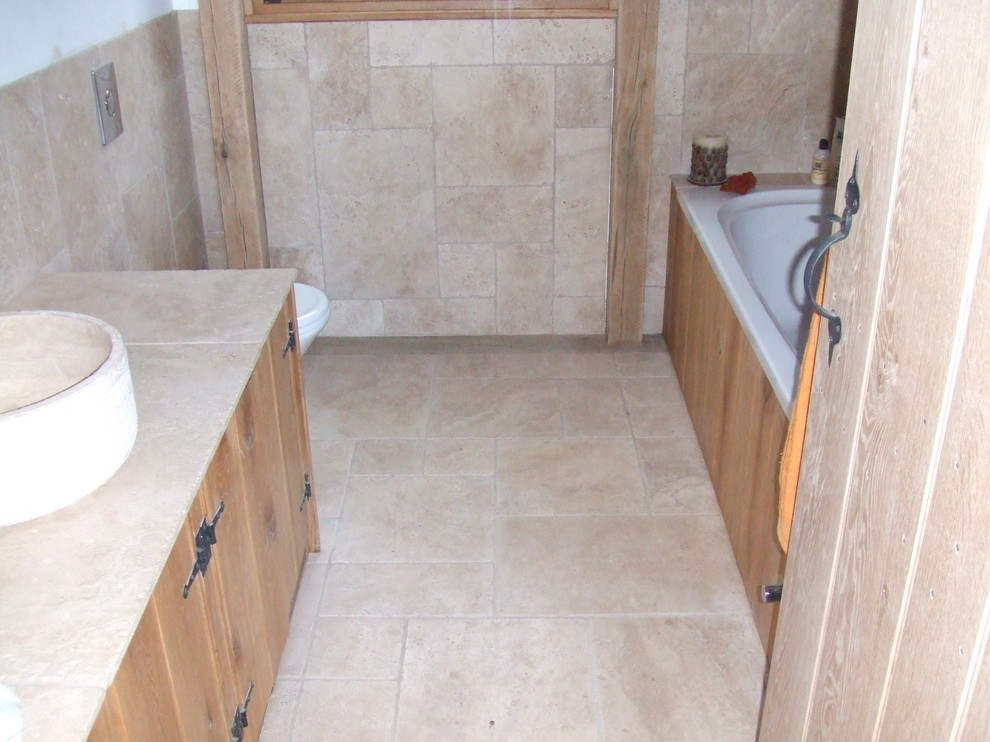 Mid-sized traditional bathroom in Other with a vessel sink, furniture-like cabinets, medium wood cabinets, a drop-in tub, a wall-mount toilet, beige tile, stone tile, beige walls and travertine floors.