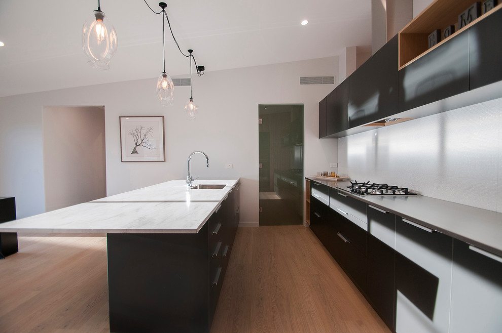 Photo of a mid-sized modern galley eat-in kitchen in Other with a single-bowl sink, black cabinets, solid surface benchtops, white splashback, ceramic splashback, stainless steel appliances, light hardwood floors, with island and beige floor.