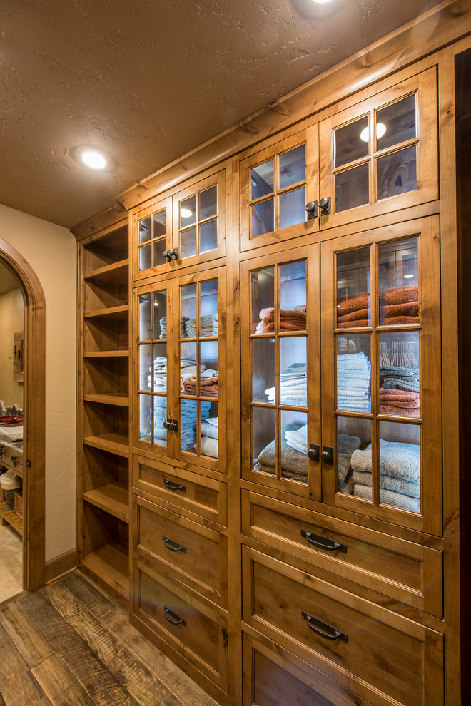 This is an example of a mid-sized country gender-neutral walk-in wardrobe in Other with recessed-panel cabinets, medium wood cabinets and dark hardwood floors.