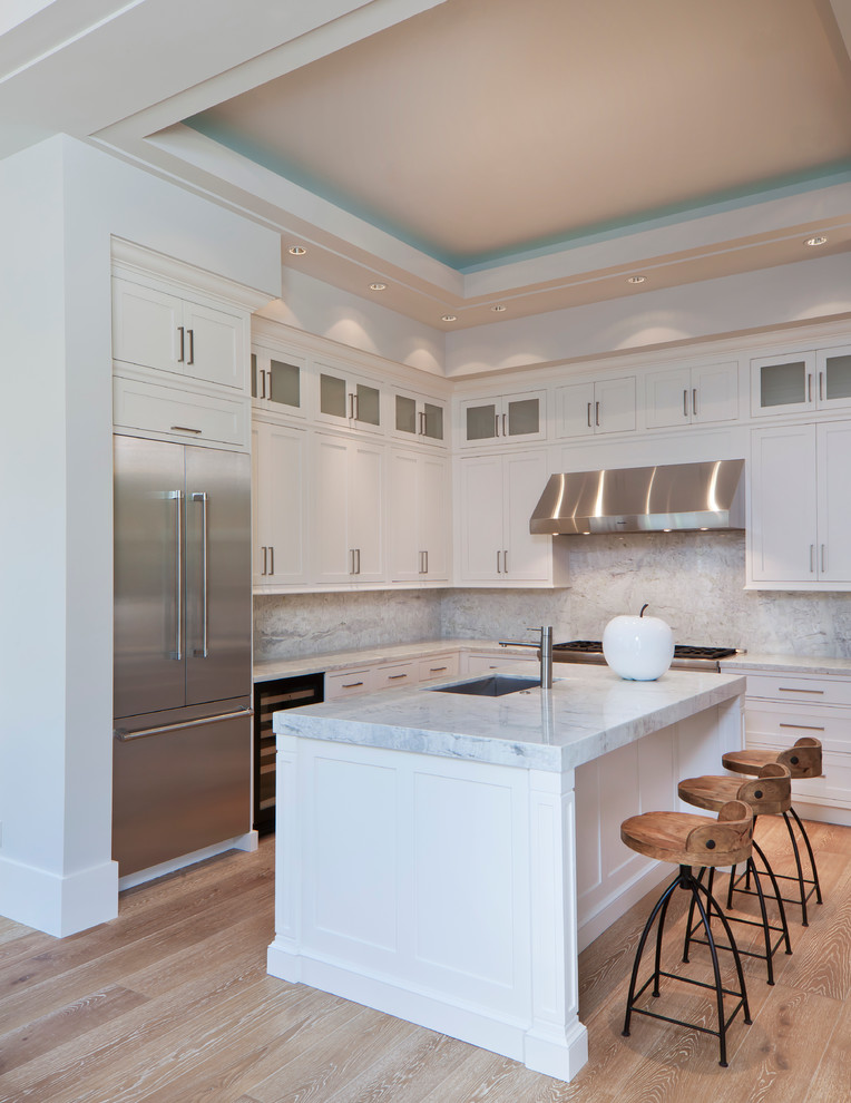 Large transitional l-shaped light wood floor and tray ceiling open concept kitchen photo in Miami with an undermount sink, shaker cabinets, white cabinets, quartz countertops, gray backsplash, quartz backsplash, stainless steel appliances, an island and gray countertops