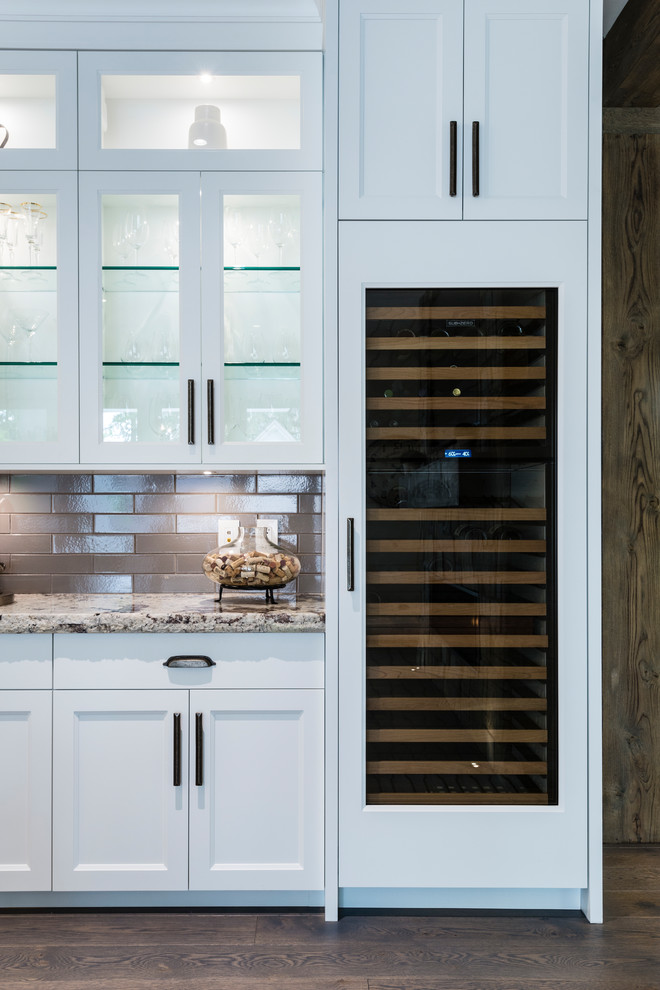Inspiration for an expansive traditional u-shaped open plan kitchen in Vancouver with medium hardwood floors, brown floor, a farmhouse sink, recessed-panel cabinets, white cabinets, granite benchtops, grey splashback, porcelain splashback, stainless steel appliances and with island.