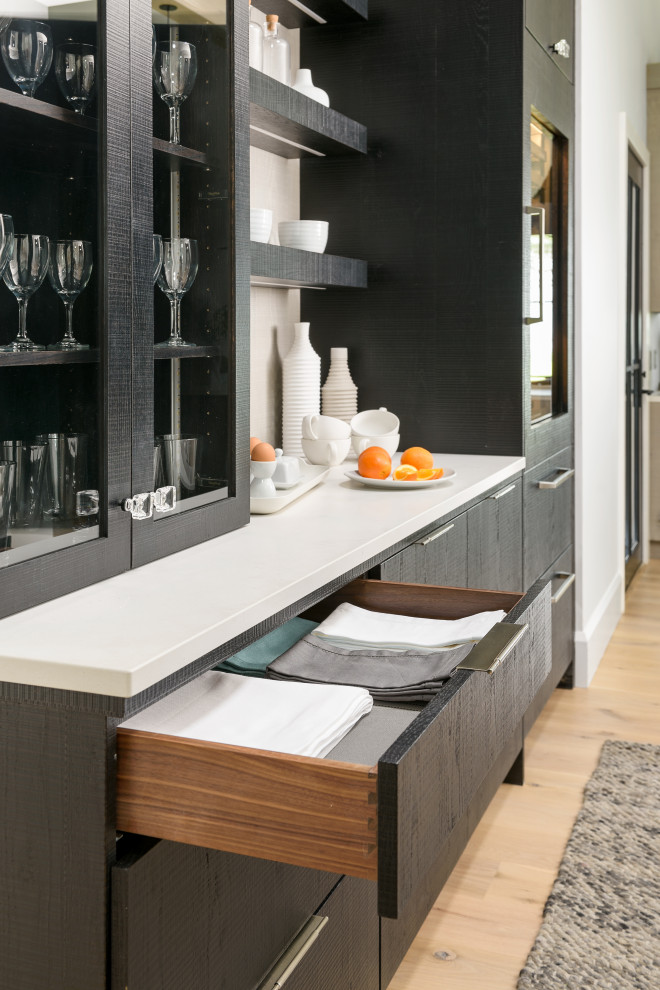 Photo of a large contemporary single-wall home bar in New York with flat-panel cabinets, black cabinets, quartzite benchtops, grey splashback, light hardwood floors, beige floor and white benchtop.