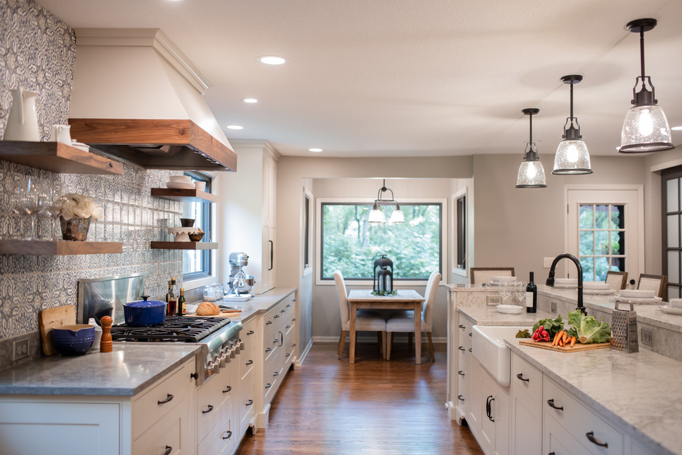 This is an example of a large country galley eat-in kitchen in Minneapolis with a farmhouse sink, beaded inset cabinets, white cabinets, quartz benchtops, blue splashback, terra-cotta splashback, stainless steel appliances, medium hardwood floors, with island, brown floor and grey benchtop.