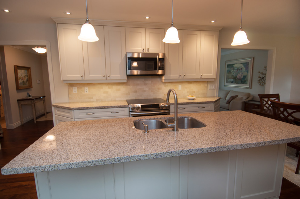 Example of a mid-sized transitional l-shaped dark wood floor eat-in kitchen design in Toronto with a double-bowl sink, shaker cabinets, white cabinets, granite countertops, beige backsplash, ceramic backsplash, stainless steel appliances and an island