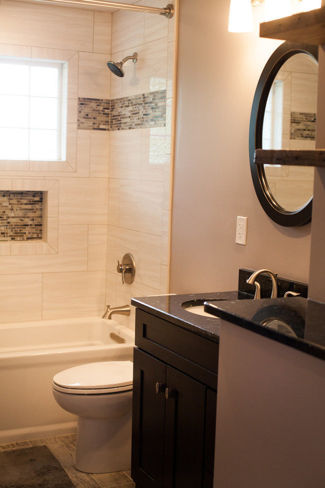 Design ideas for a small transitional 3/4 bathroom in Nashville with shaker cabinets, dark wood cabinets, an alcove tub, a shower/bathtub combo, a two-piece toilet, beige tile, porcelain tile, beige walls, laminate floors, an undermount sink, granite benchtops, beige floor, a shower curtain and black benchtops.