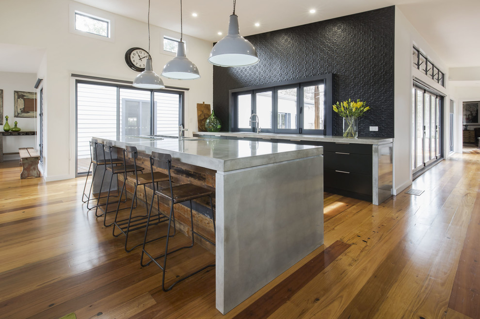 Photo of a mid-sized contemporary single-wall open plan kitchen in Sydney with an undermount sink, flat-panel cabinets, black cabinets, concrete benchtops, black splashback, metal splashback, stainless steel appliances, medium hardwood floors and with island.