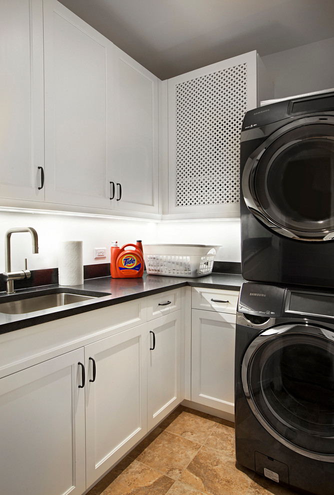 Dedicated laundry room - mid-sized traditional l-shaped porcelain tile dedicated laundry room idea in Chicago with an undermount sink, recessed-panel cabinets, white cabinets, granite countertops, white walls, a stacked washer/dryer and black countertops