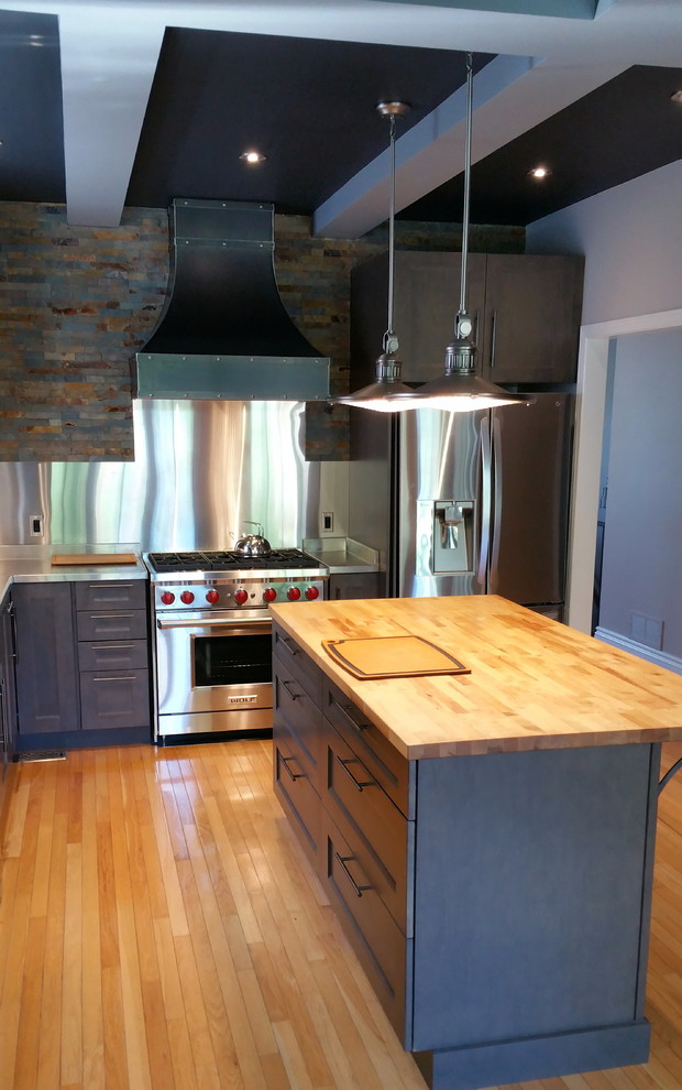 Mid-sized industrial l-shaped separate kitchen in Ottawa with a double-bowl sink, shaker cabinets, grey cabinets, stainless steel benchtops, metallic splashback, stone tile splashback, stainless steel appliances, light hardwood floors and with island.