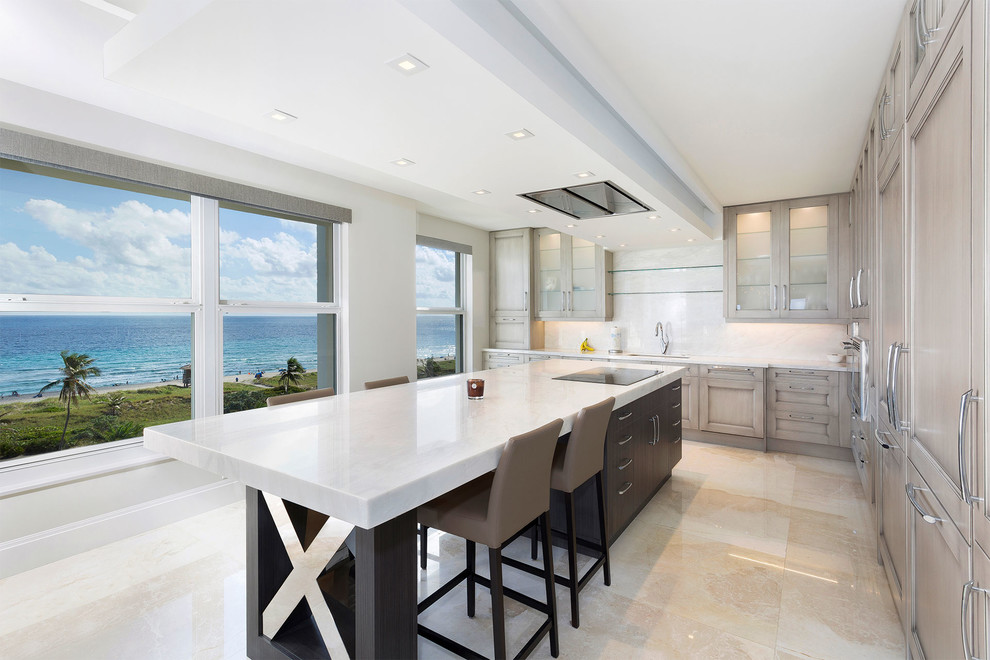 This is an example of a small transitional l-shaped open plan kitchen in Miami with recessed-panel cabinets, white splashback, with island, beige floor, white benchtop, a triple-bowl sink, marble benchtops, marble splashback, stainless steel appliances, porcelain floors and grey cabinets.