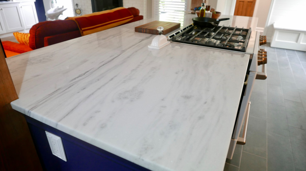 Example of a mid-sized transitional galley porcelain tile and black floor eat-in kitchen design with a farmhouse sink, shaker cabinets, blue cabinets, marble countertops, white backsplash, subway tile backsplash, white appliances, an island and multicolored countertops