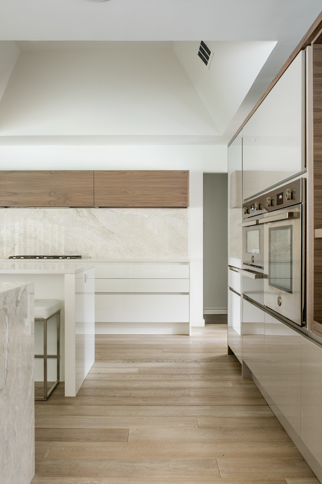 This is an example of a mid-sized contemporary l-shaped eat-in kitchen in Dallas with an undermount sink, flat-panel cabinets, white cabinets, quartz benchtops, white splashback, stone slab splashback, stainless steel appliances, light hardwood floors and multiple islands.
