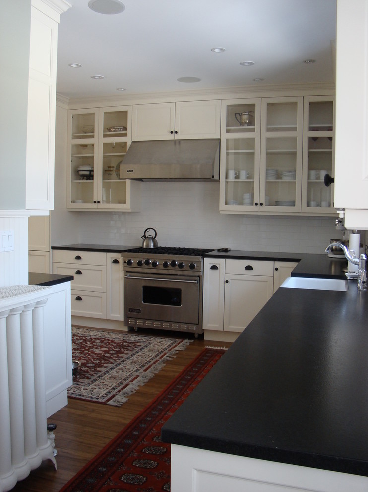 Design ideas for a large traditional l-shaped eat-in kitchen in Portland Maine with a farmhouse sink, glass-front cabinets, white cabinets, granite benchtops, white splashback, subway tile splashback, stainless steel appliances, bamboo floors and no island.
