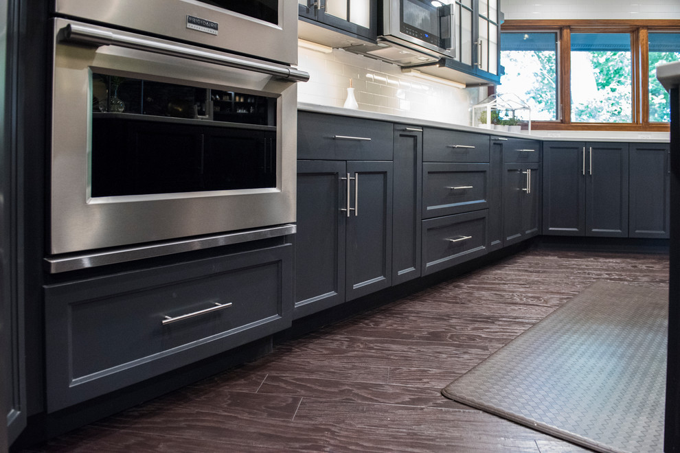 Example of a large transitional u-shaped dark wood floor kitchen design with an undermount sink, beaded inset cabinets, gray cabinets, quartz countertops, white backsplash, subway tile backsplash, stainless steel appliances and an island