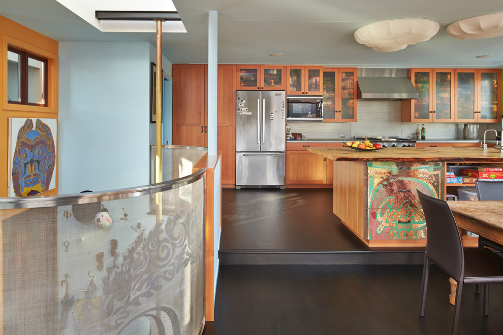 Eclectic l-shaped open plan kitchen in Seattle with glass-front cabinets, medium wood cabinets, wood benchtops, grey splashback and stainless steel appliances.