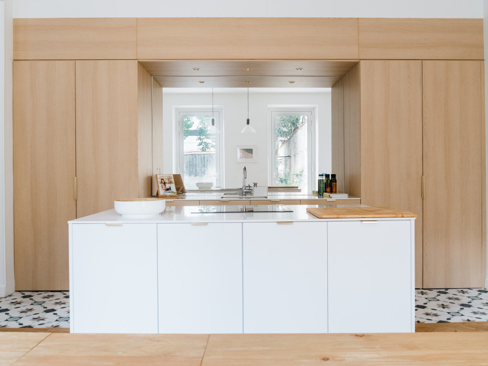 Foto på ett stort funkis vit linjärt kök med öppen planlösning, med en undermonterad diskho, luckor med infälld panel, skåp i ljust trä, granitbänkskiva, stänkskydd med metallisk yta, spegel som stänkskydd, integrerade vitvaror, cementgolv, en köksö och flerfärgat golv